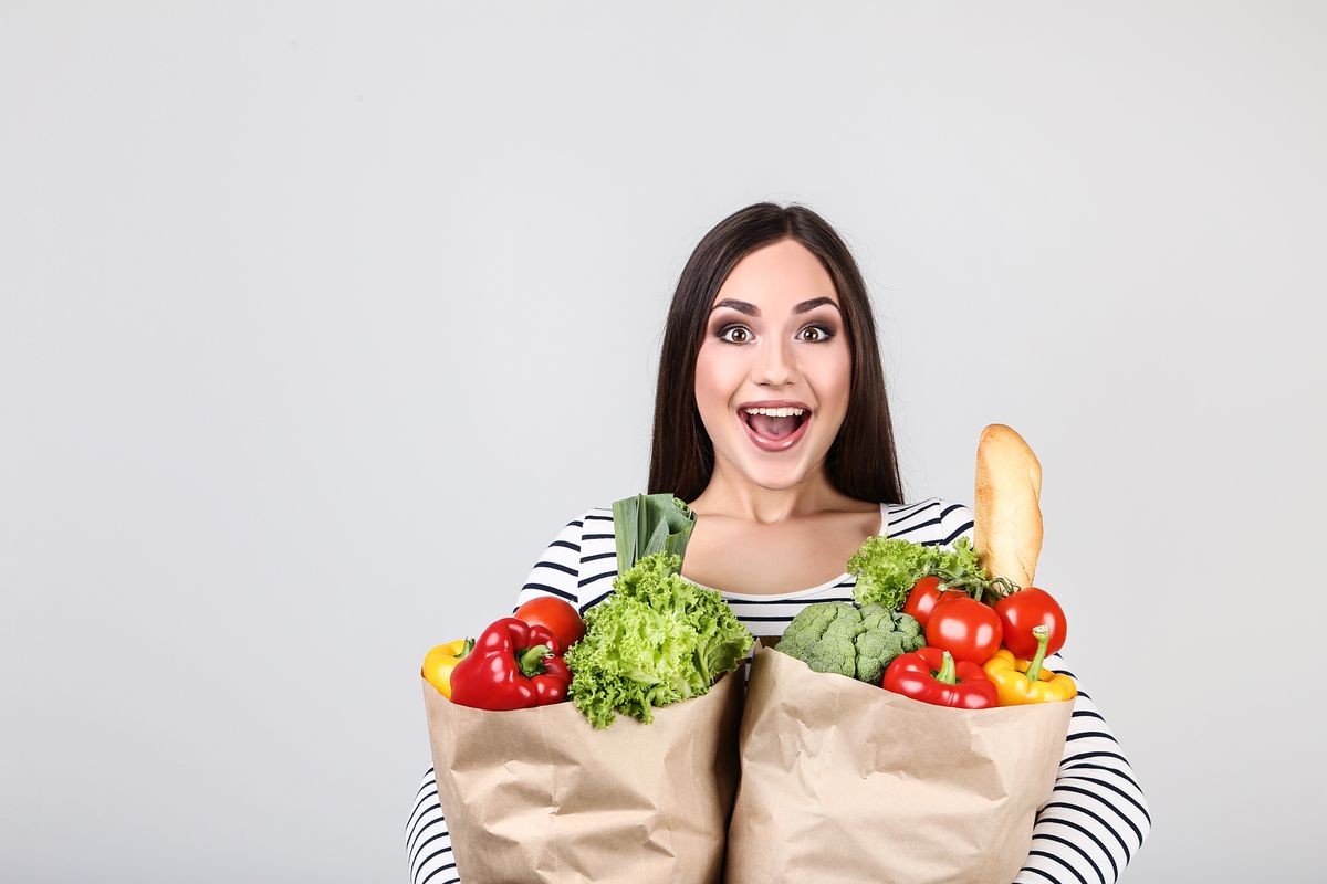 Beautiful woman holding grocery shopping bags on grey background